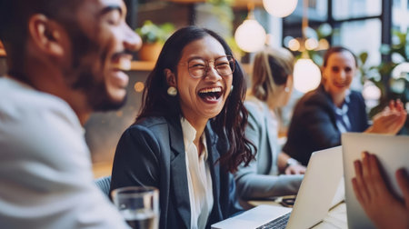 Happy businesspeople laughing while collaborating on a new project in an office. Group of diverse businesspeople using a laptop while working together in a modern workspace.の素材
