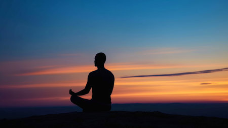 A serene scene of an individual practicing meditation at sunrise, their silhouette against the calming hues of the morning sky, embodying tranquility and mindfulness.の素材