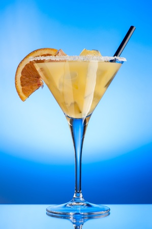 Glass of margarita with ice cubes and a slice of orange over a light blue backgroundの写真素材