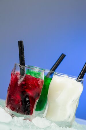 Three frozen shots, green white and red, with drinking straws over a light blue backgroundの写真素材