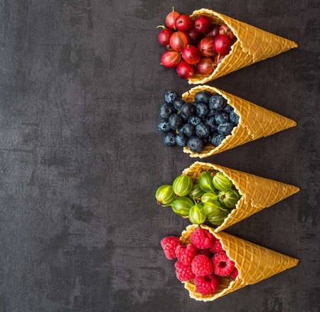 Berries. Raspberries, blackberries, blueberries in waffle cones on a wodden background. Healthy food concept.Gray stone background.Top view.の写真素材