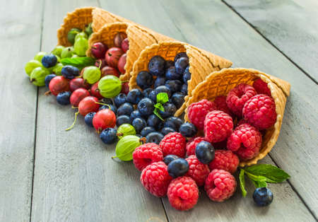 Berries. Raspberries, blackberries, blueberries in waffle cones on a wodden background. Healthy food conceptの写真素材