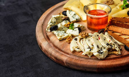 Cheese plate: Parmesan, cheddar, gouda, mozzarella and other with basil on wooden board on dark background with place for text.Honey and Crackersの写真素材