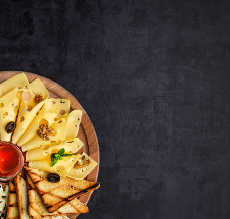 Cheese plate: Parmesan, cheddar, gouda, mozzarella and other with basil on wooden board on dark background with place for text.Honey and Crackersの写真素材