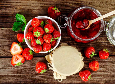 Homemade strawberry jam or marmalade in the glass jar and the basket of ripe strawberries on the...