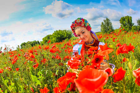 beautiful girl in Ukrainian national costume walking through poppy field dramatic sky