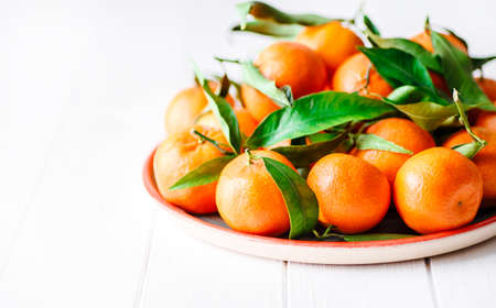 Tangerines (oranges, clementines, citrus fruits) with green leaves over wooden background with copy space.bowl of fresh mandarinsの写真素材
