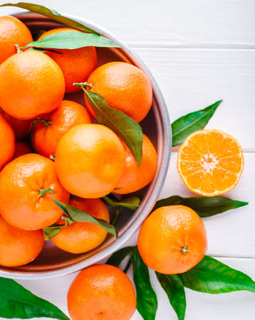 Tangerines (oranges, clementines, citrus fruits) with green leaves over wooden background with copy space.bowl of fresh mandarinsの写真素材