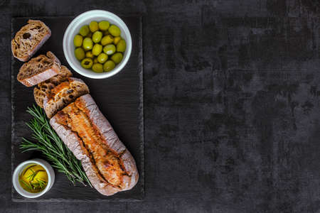 Ciabatta bread on black slate board with herbs and olives, top view,sliced bread Ciabatta and rosemaryの写真素材