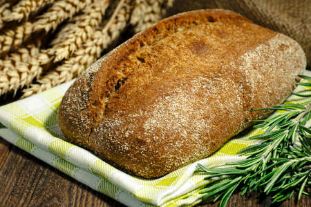 Sliced freshly baked ciabatta bread on wooden cutting board on rustic table with rosemary, salt,...