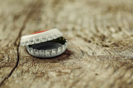 bottle cap from a beer bottle on wooden background. several beer lids lie in pile, behind them...