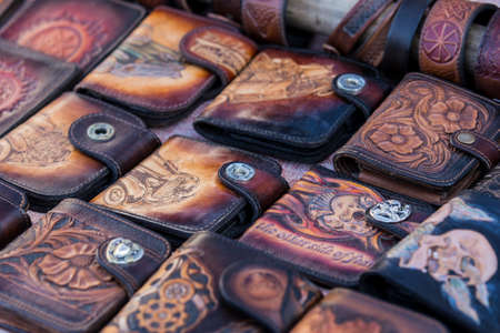 Leather goods: bags, purses, purses are on the trading table in the market of handmade products.Top view of leather wallet with money on wooden table. Leather craft.Biker theme.の写真素材