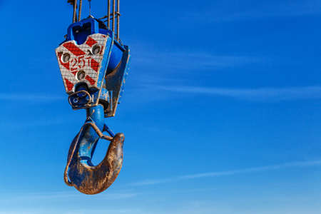 Crane hook with red and white stripes hanging, blue sky with white clouds background, detail