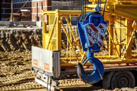 Mobile construction cranes with yellow telescopic arms and big tower cranes in sunny day. Heavy industry.Crane hook with red and white stripes hangingの写真素材