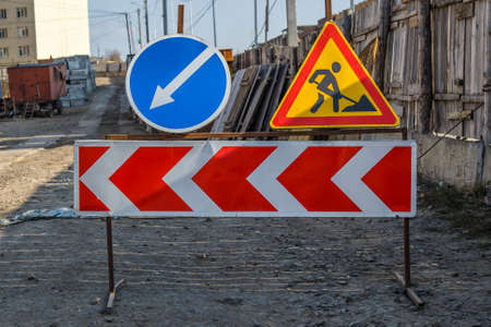 Work in progress. Roadworks, road signs. Men at work. Some signs signage for work in progress on urban street. Barriers and road signs. Silhouette of a worker at work. Right arrow.の写真素材