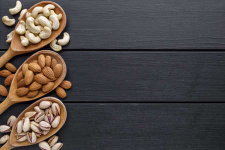 nuts in wooden bowl. Assortment of nuts - cashew, hazelnuts, walnuts, pistachio, pecans, pine nuts, peanut, raisins  on black background.Healthy snack, vegetarian food, Top view.の写真素材