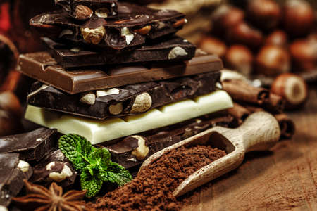 Stack of chocolate slices with mint leaf on a wooden table. Assortment of fine chocolates in white,...