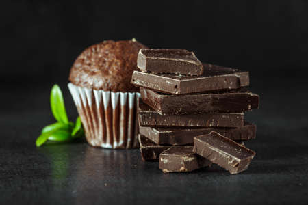 Chocolate cupcake with icing and chocolate bar in Dark lighting, Homemade delicious chocolate muffin on wooden background close-upの写真素材