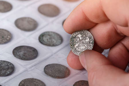 Numismatics. Old collectible coins made of silver on a wooden table. A collector holds an old coin.の写真素材