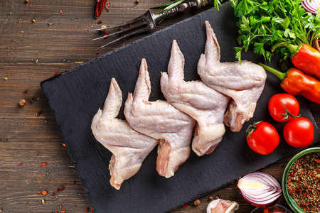 Shooting for the catalog.Chicken wings lie on a wooden board with vegetables and spices on a black background.Top viewの写真素材