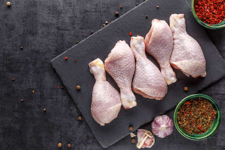 Shooting for the catalog. Raw chicken legs with spices and vegetables on a wooden cutting board. Black background. Top viewの写真素材