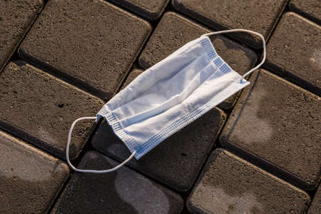 Medical face mask on the floor in the street.Used Surgical masks haphazardly strewn on pavement.Improperly discarding used face mask. Lost face mask at pavementの写真素材