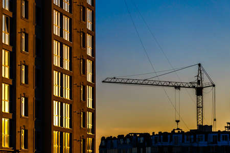 Big crane silhouette and many workers building new construction under a beautiful colorful sunset...