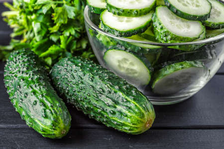 Cucumber on dark wood texture background. Cucumbers harvest in summer. Cucumbers for salads or canning. Summer vegetables.Slices of fresh cucumbers in a bowl.