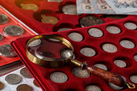 Numismatics. Old collectible coins made of silver on a wooden table.Coins in the album.Collection of old coins. Magnifying glassの写真素材