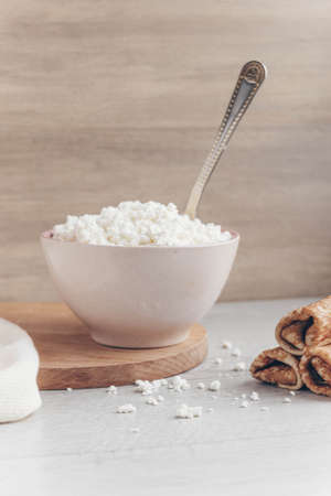 On the table is a large bowl of fresh cottage cheese. Next to it are pancakes with cottage cheese filling. Soft picture, slightly out of focus.の写真素材