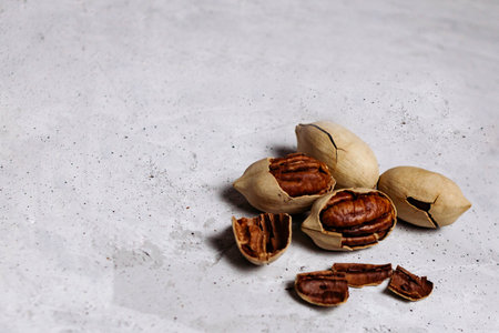 Cracked pecans lie in a heap on a gray concrete background. There is room for text.