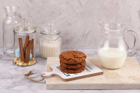 A stack of delicious chocolate cookies on a board with a jug of milkの写真素材