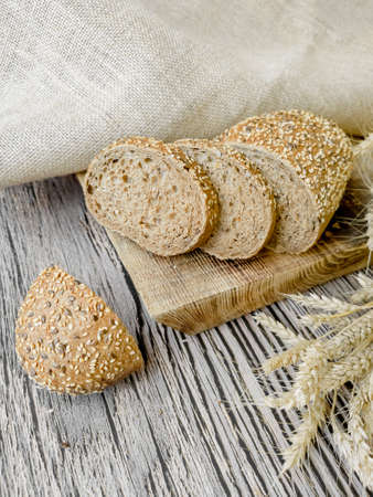 Freshly baked whole-grain, yeast-free bread lies on a wooden board, cut into pieces. The loaf is...