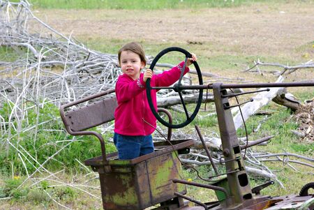 A little girl standing in the seat of an old tractorの写真素材