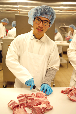 A young male butcher cutting meat in an industrial kitchenの写真素材