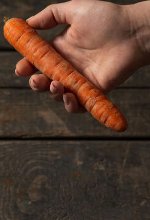Carrot in hand on wooden texture background. Concept: market, vegetables, carrotsの写真素材
