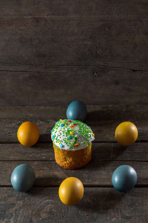 Painted eggs for Easter in the colors of the flag of Ukraine and Easter cake. Yellow and blue (cyan). On wood texture. Concept: food, holiday, war in Ukraineの写真素材