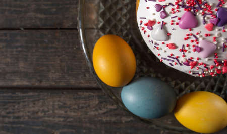 Easter cake in a transparent dish, around painted eggs in the colors of the flag of Ukraine. Yellow and blue (cyan). On wood texture. Concept: food, holiday, war in Ukraineの写真素材
