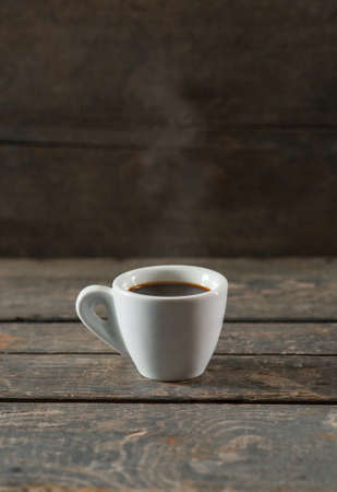 Hot black coffee or espresso in white ceramic cup on wooden texture background with steamの写真素材