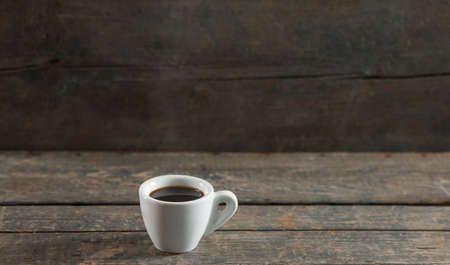 Hot black coffee or espresso in white ceramic cup on wooden texture background with steamの写真素材