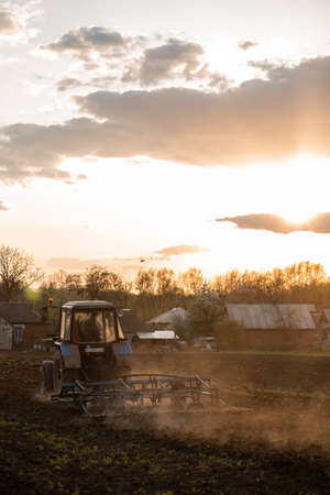 The tractor cultivates the land in the field at sunset. Dust. industry, agricultureの写真素材