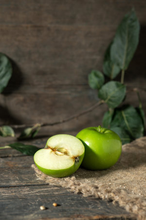 Green apple whole and cut half with leaves on burlap on wooden planksの写真素材