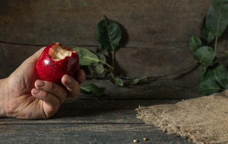 In hand a bitten red apple with leaves on burlap on wooden planksの写真素材