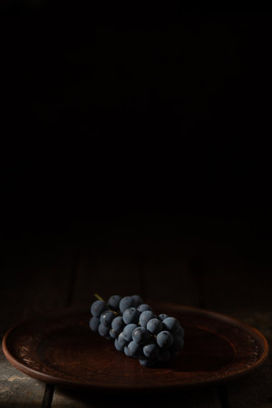 blue grapes on a clay plate on a wooden tableの写真素材