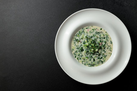 Cold soup with fresh cucumbers, sausage, broth and sour cream in a plate-hat on a black background. A traditional dish is okroshka.の写真素材