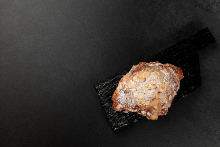 Almond croissant. puff pastry, delicate frangipane cream with almonds, enriched with butter. On top, the croissant has a hint of almond flakes and powdered sugar. on a black cutting boardの写真素材