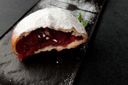 An appetizing donut with strawberries sprinkled with powdered sugar on a black rectangular plate on a gray backgroundの写真素材