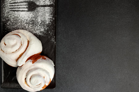 Fragrant cinnabons with cream on a black rectangular plate on a gray backgroundの写真素材