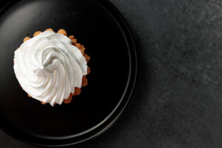 cupcake with whipped cream in a black round plate on a black backgroundの写真素材