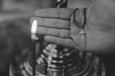 Baptism cross in a man's hand in front of candles, black and white photoの写真素材